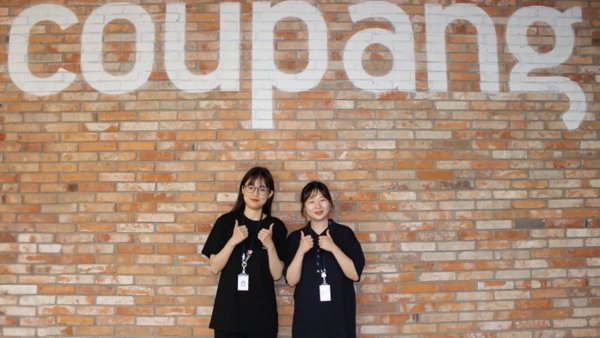 two women standing in front of a brick wall